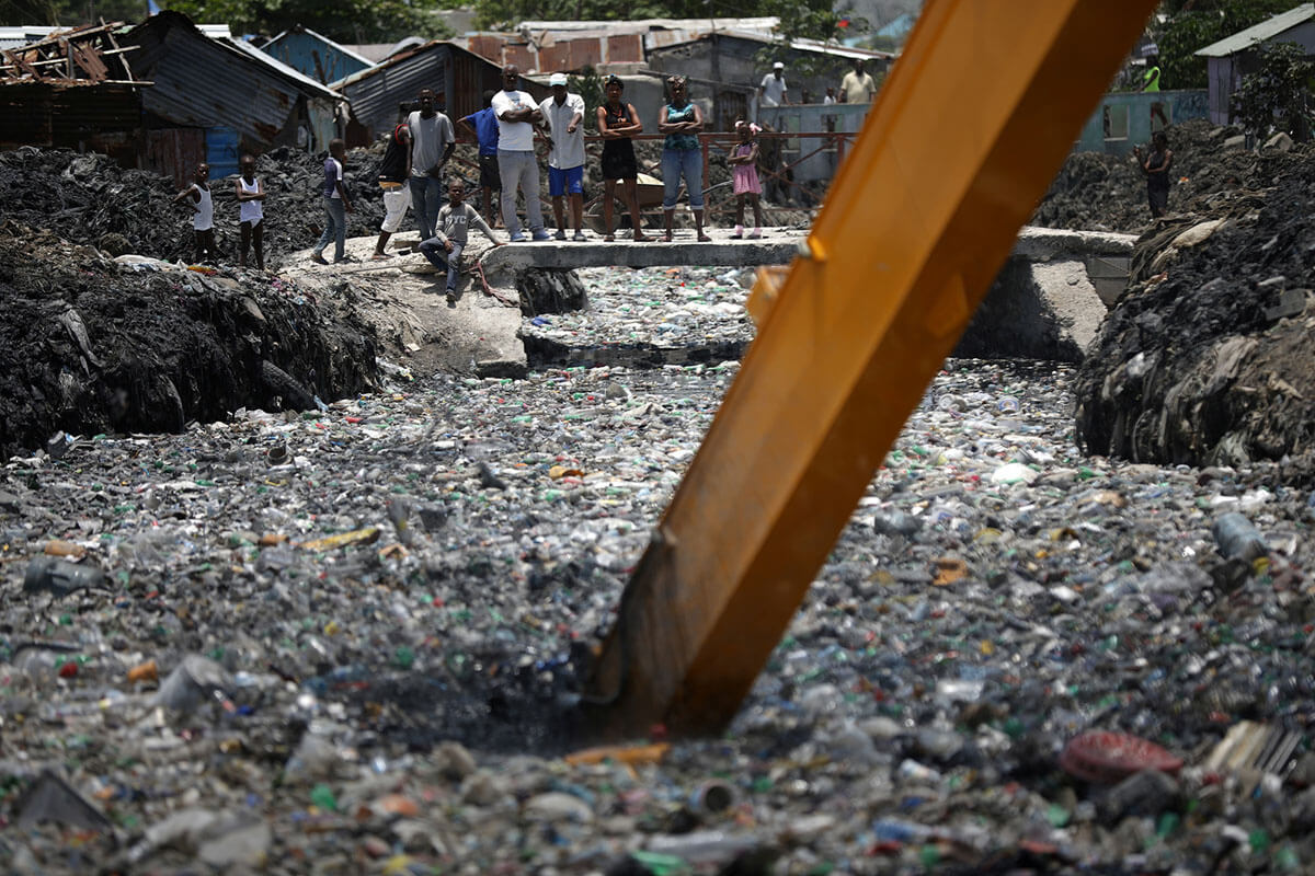 Orang-orang menonton ekskavator yang sedang memungut sampah dari sungai di Cite Soleil, Port-au-Prince, Haiti, 21 Mei 2018